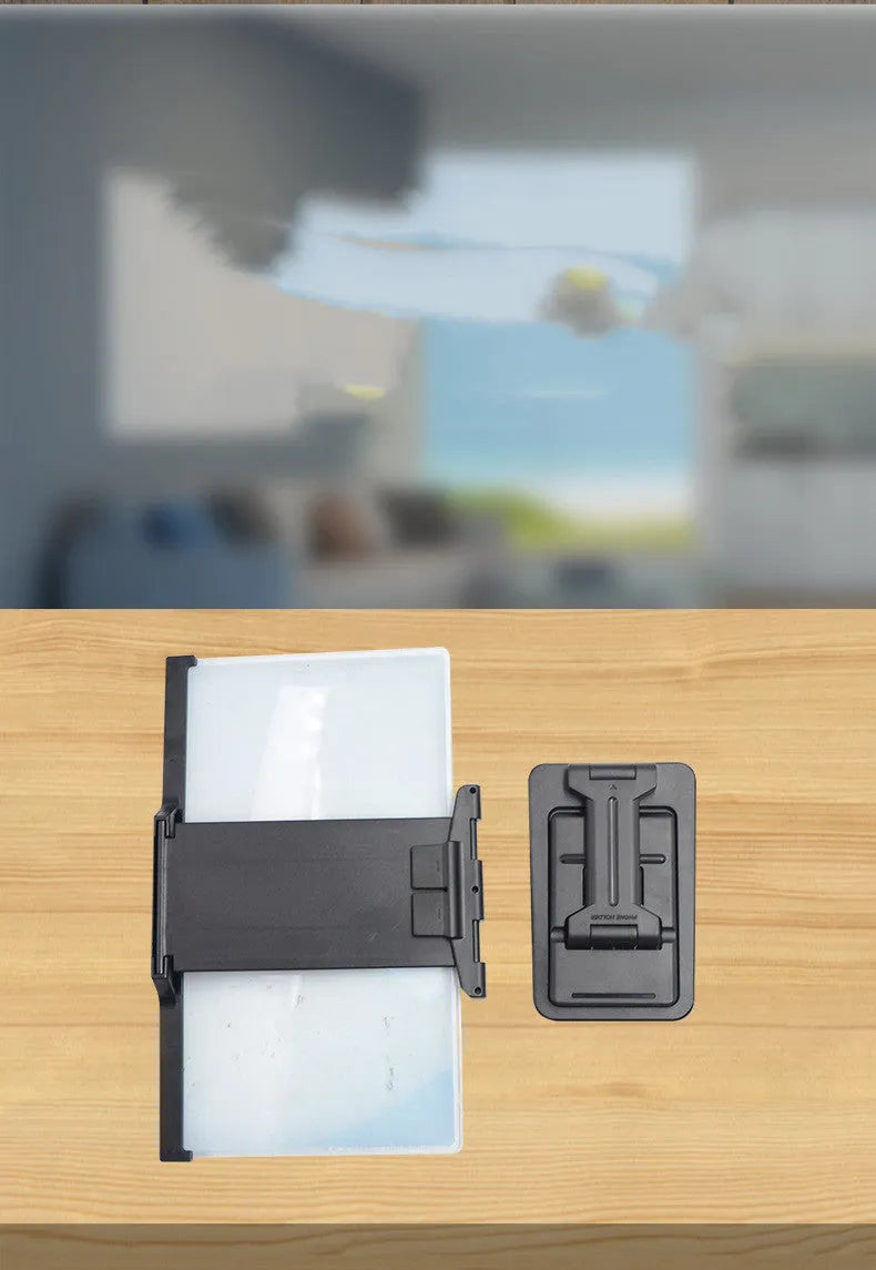 Black detachable mobile phone screen amplifier and folding holder shown on a desk next to a phone.