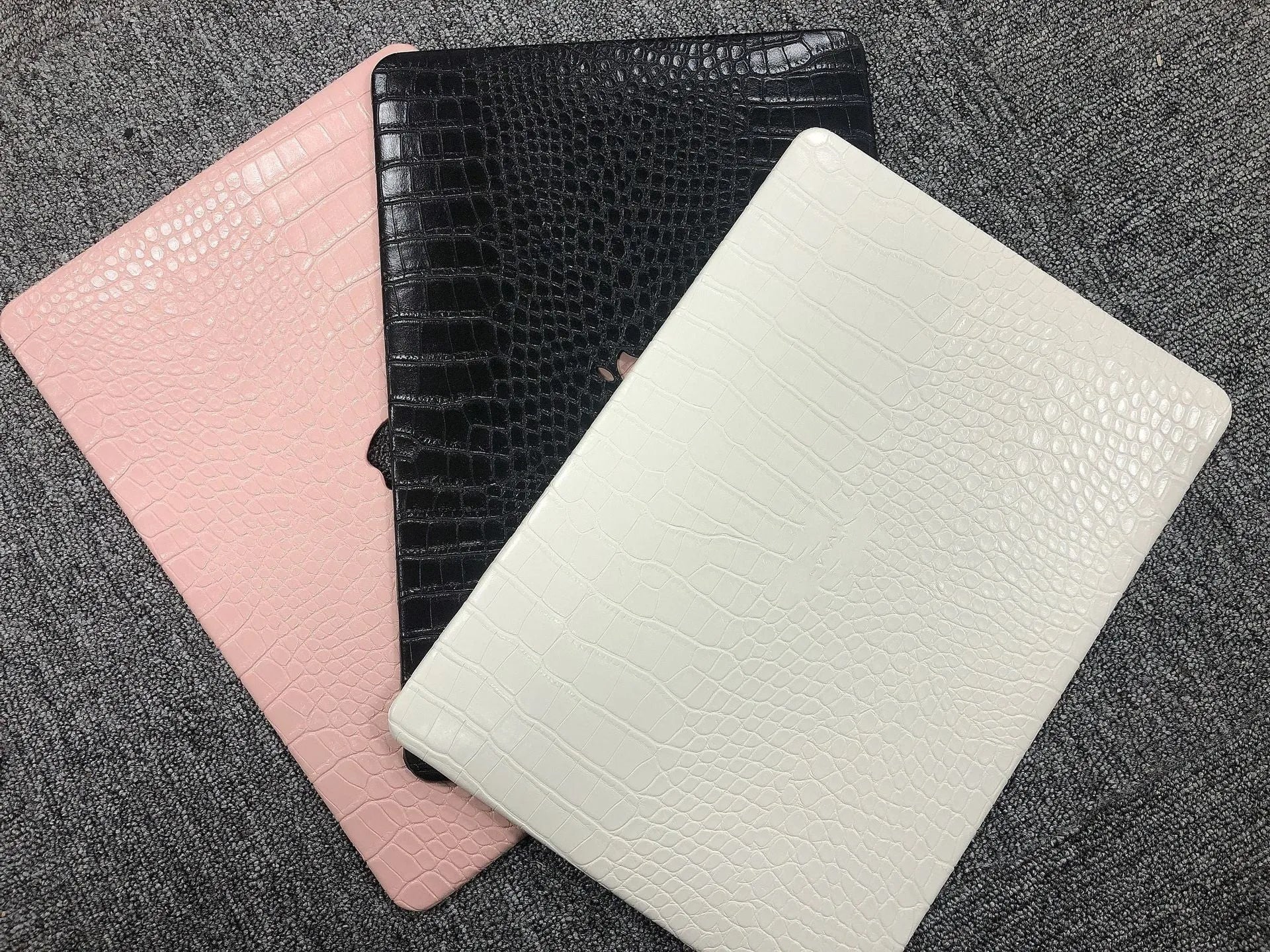 Black MacBook protective case with crocodile texture and visible Apple logo through a cutout.