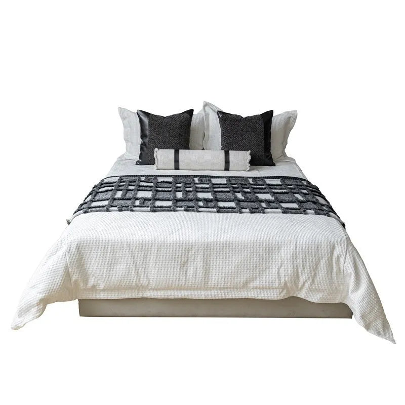 Modern minimalist grey and white plaid bed runner blanket set with matching pillowcase and leather round pillow on a bed.