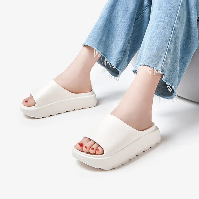 Women's beige open-toe beach slippers with a thick light-coloured sole on a wooden deck.