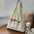 Beige canvas bag with bread patterns including croissant design, showing one-shoulder strap and structured form