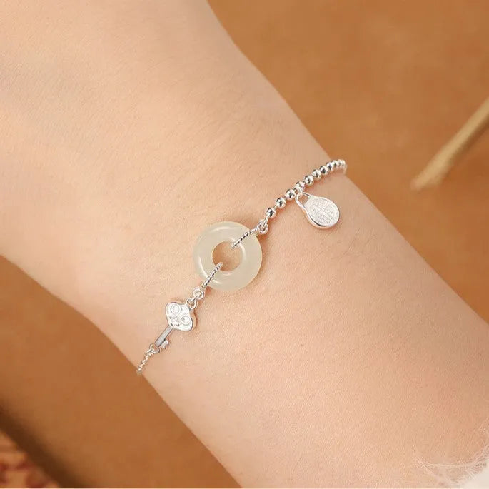 Women's silver bracelet with Hetian jade and a traditional Chinese peace buckle charm on a geometric link chain.