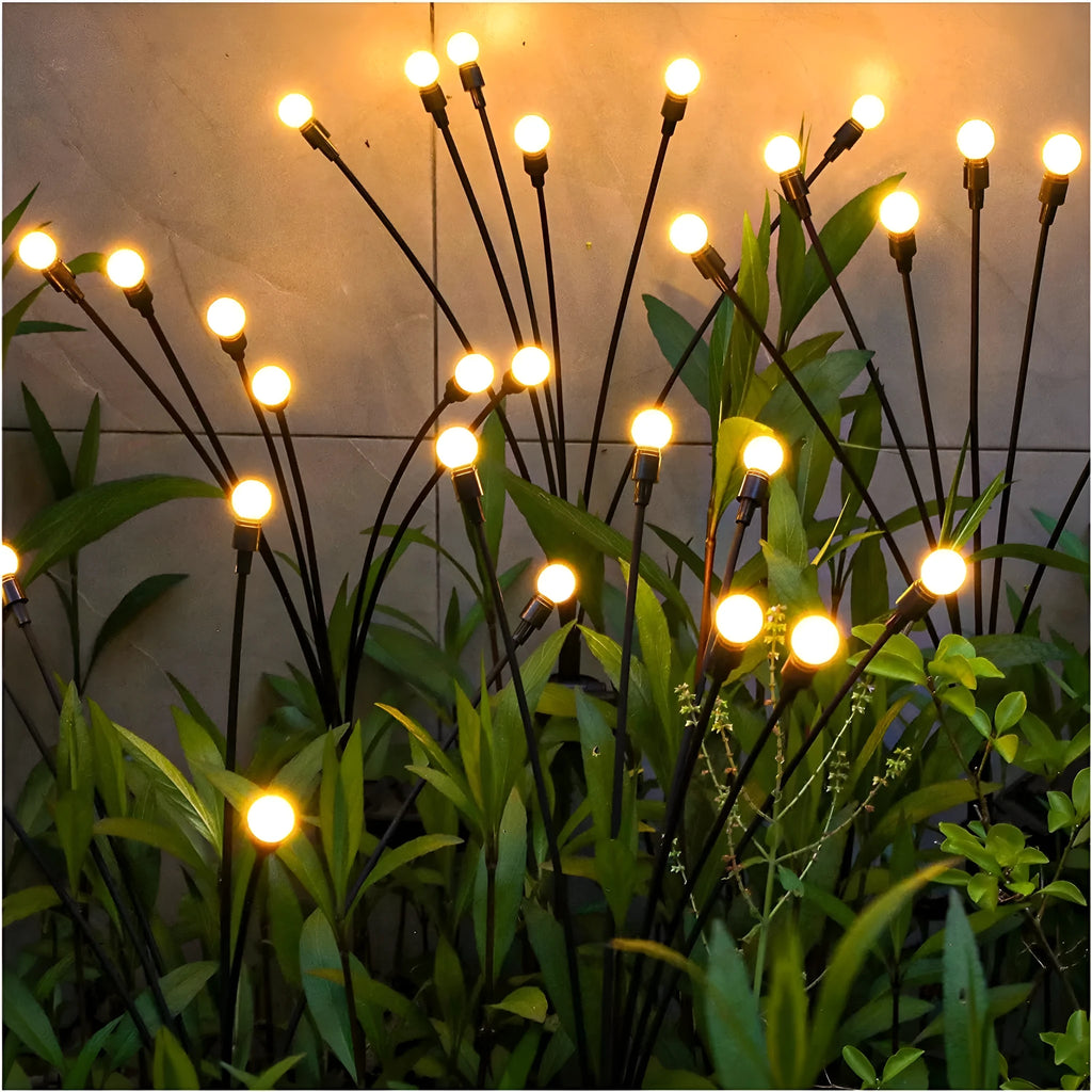 Solar-powered LED pneumatic firefly ground stake light with multiple heads on a grassy lawn.