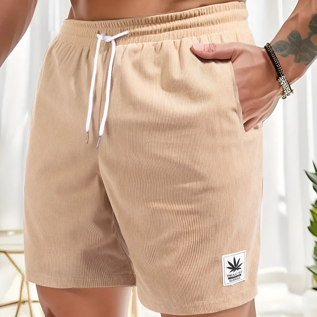 Man wearing grey straight-cut elastic drawstring summer shorts on a beach.