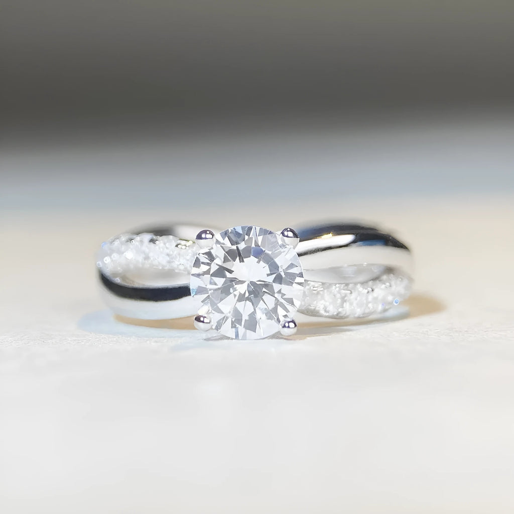 A silver moissanite ring with a 1 carat stone in a four-claw setting and a twisted geometric band.
