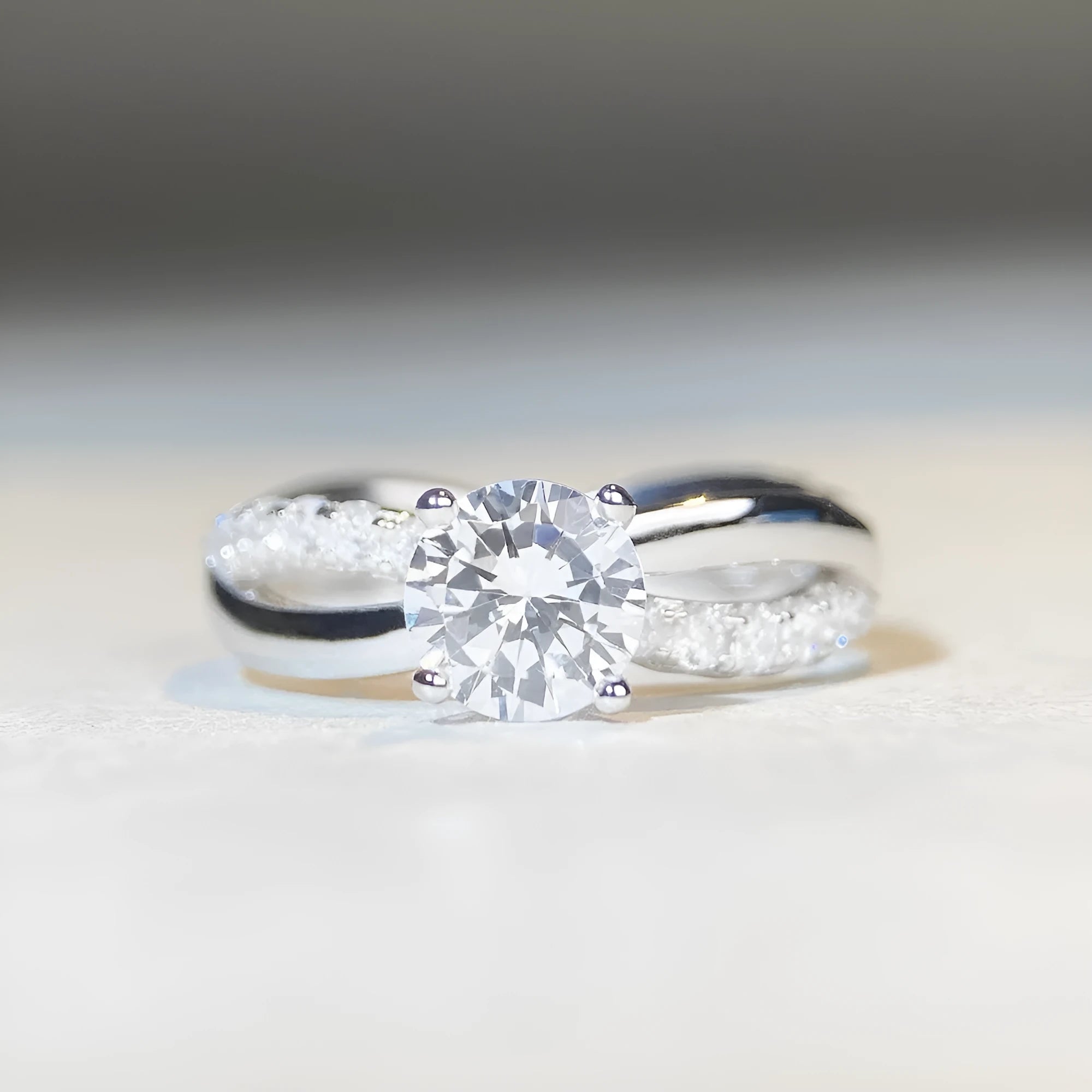 A silver moissanite ring with a 1 carat stone in a four-claw setting and a twisted geometric band.