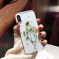 Clear soft TPU iPhone case with pink dried flowers preserved in epoxy resin on the back.