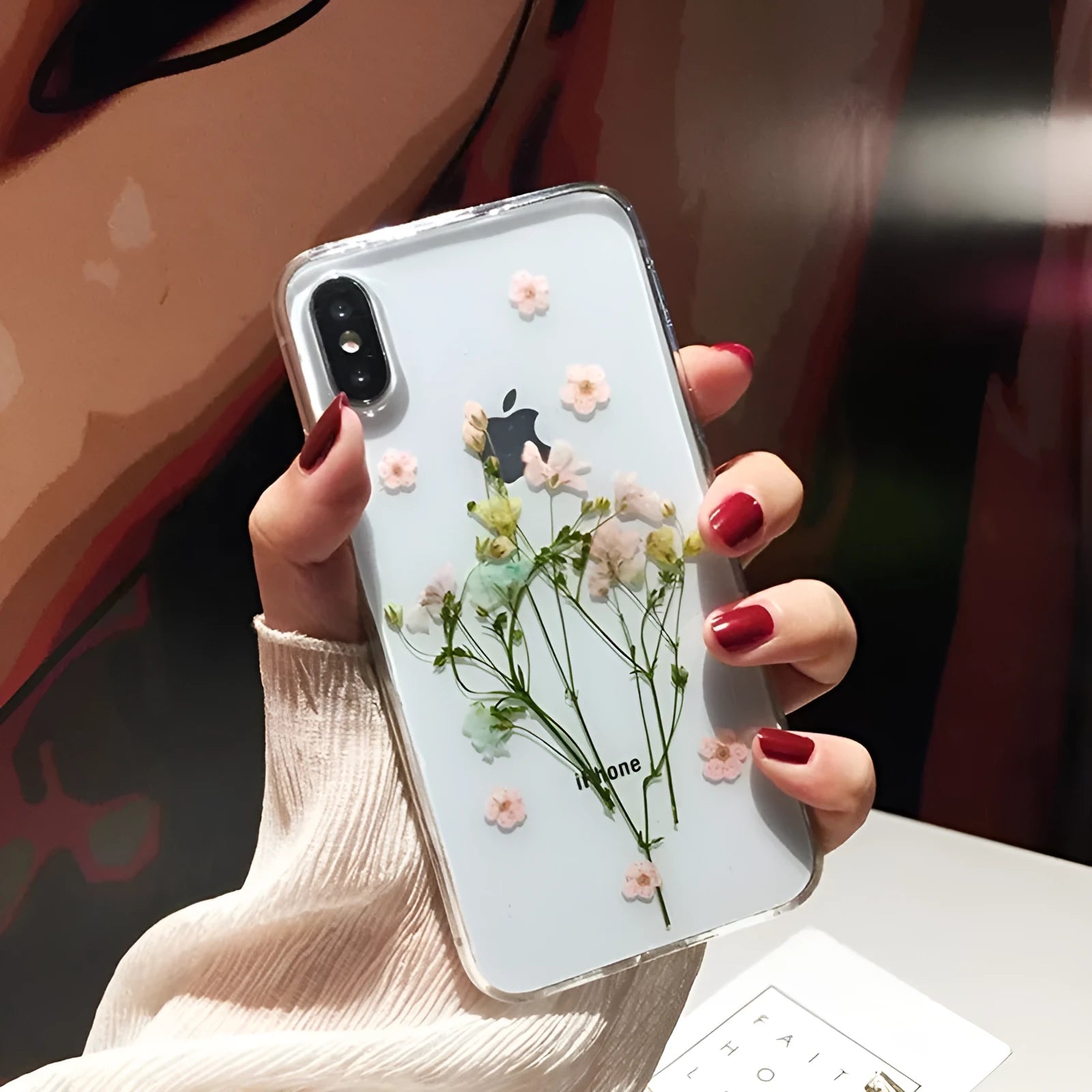 Clear soft TPU iPhone case with pink dried flowers preserved in epoxy resin on the back.