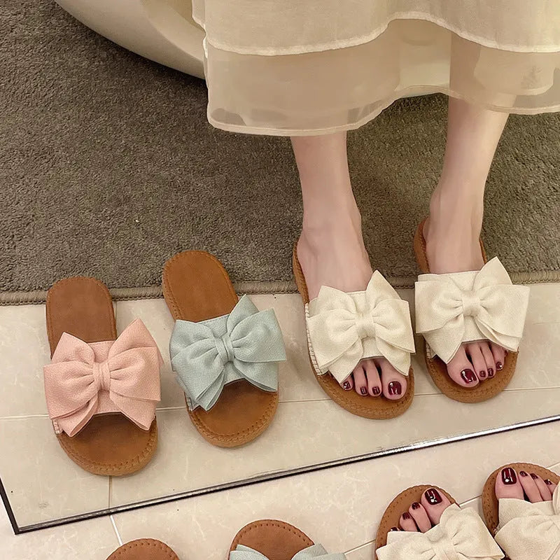 Women's beige suede slip-on sandals with a bow and flat soft rubber sole.