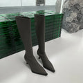 Black pointed toe below-the-knee boots on a woman, showing the back zipper and stiletto heel.