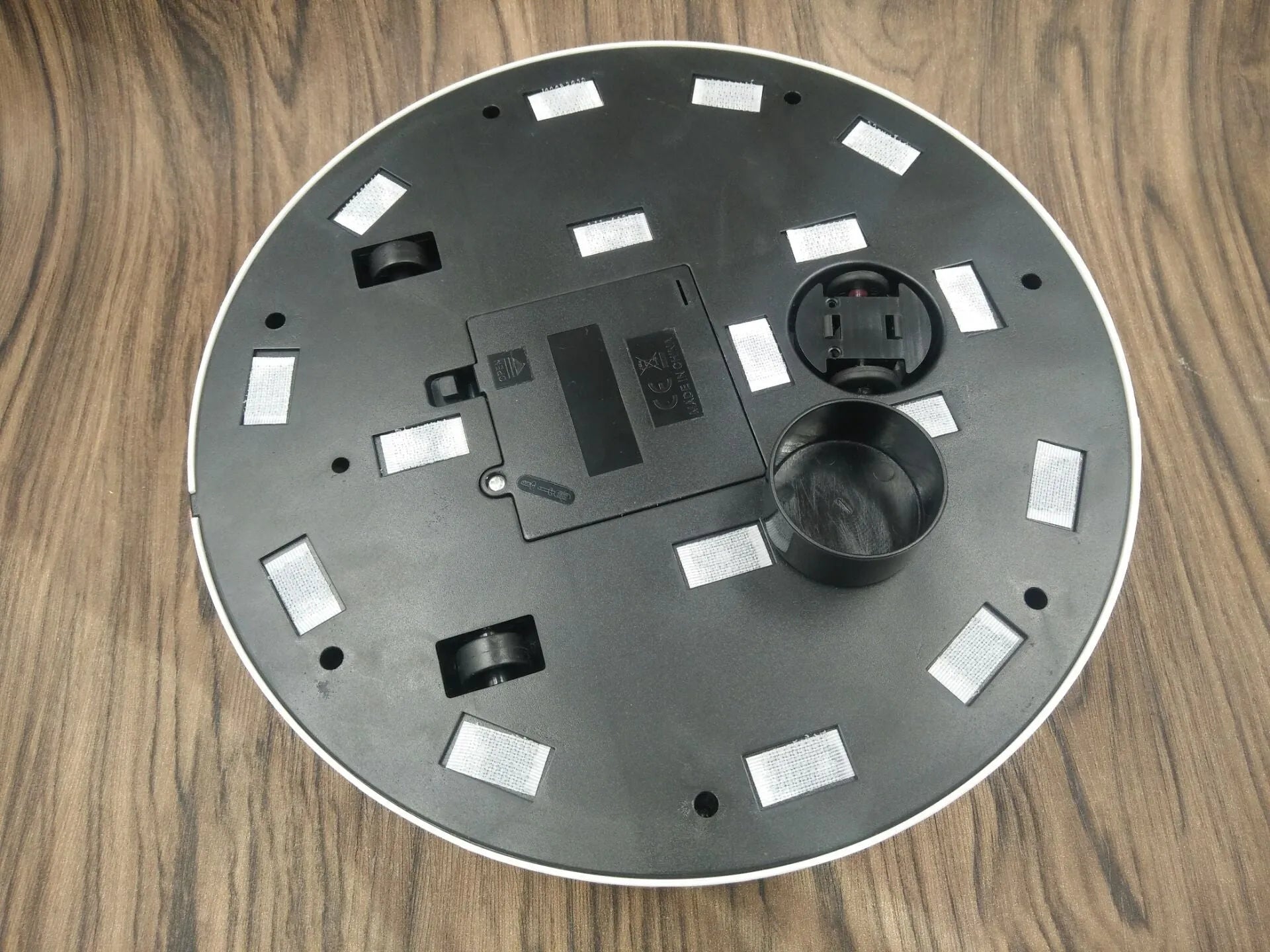 Black automatic sweeping robot on a wooden floor next to its packaging.