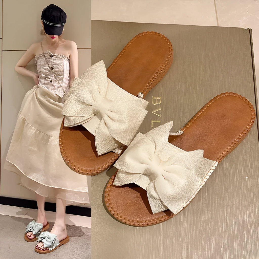 Women's beige suede slip-on sandals with a bow and flat soft rubber sole.