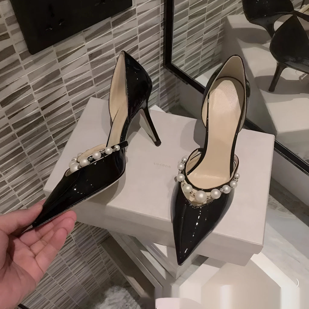 Women's black pointed toe stiletto high heels with pearl detail on patent leather-look upper.