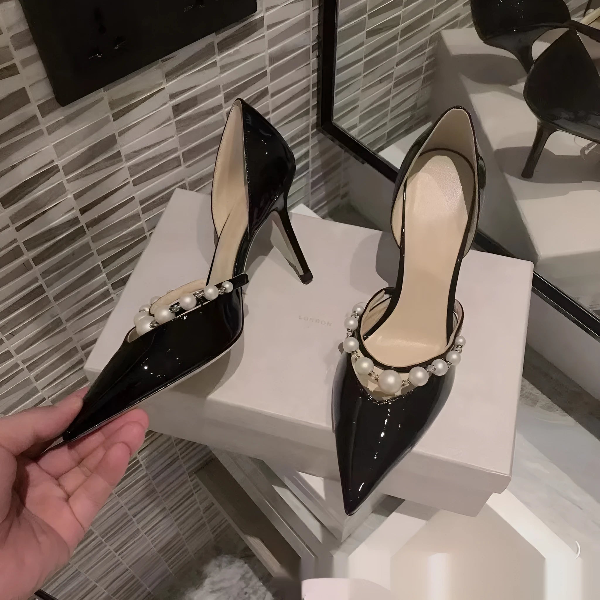 Women's black pointed toe stiletto high heels with pearl detail on patent leather-look upper.