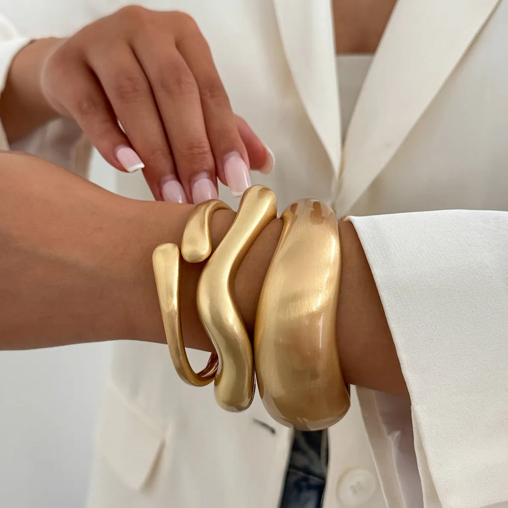 Electroplated alloy opening bracelet with elliptical motif in matte gold finish, cold wind style