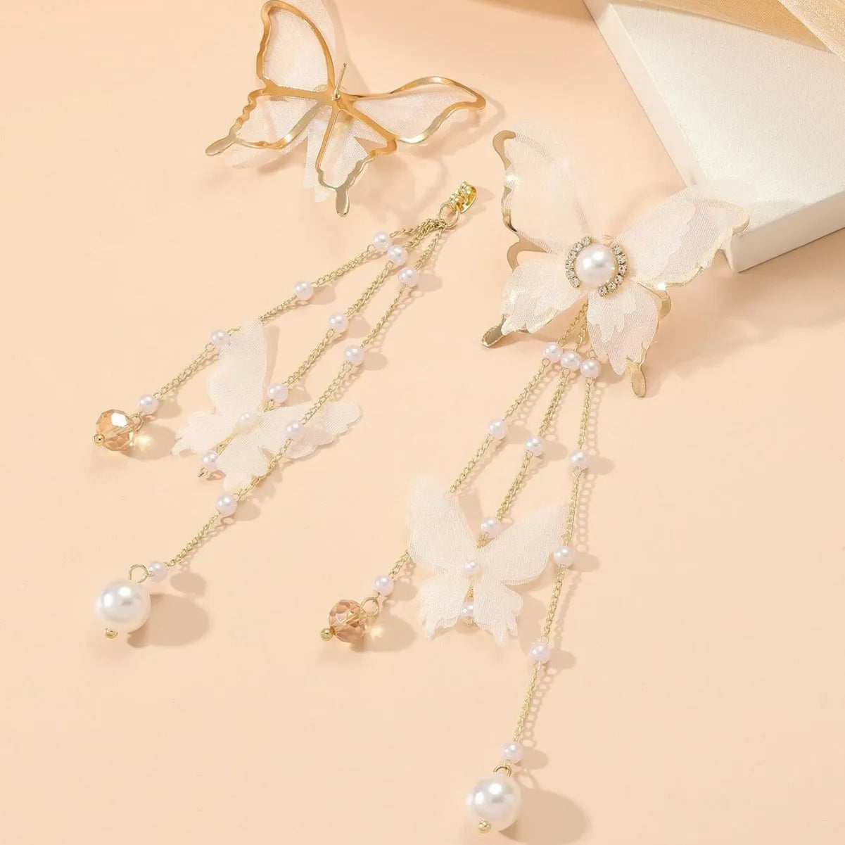Close-up of white butterfly-shaped earrings with dangling lace tassels and sparkling pearl rhinestone details.
