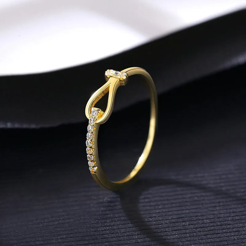 Gold electroplated silver bow ring with inlaid zirconium on pink background, front view