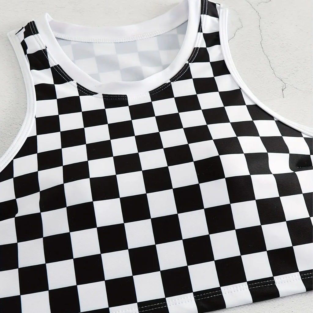 Adult woman wearing a black and white checkerboard print one-piece swimsuit with suspender straps and a backless sporty design.