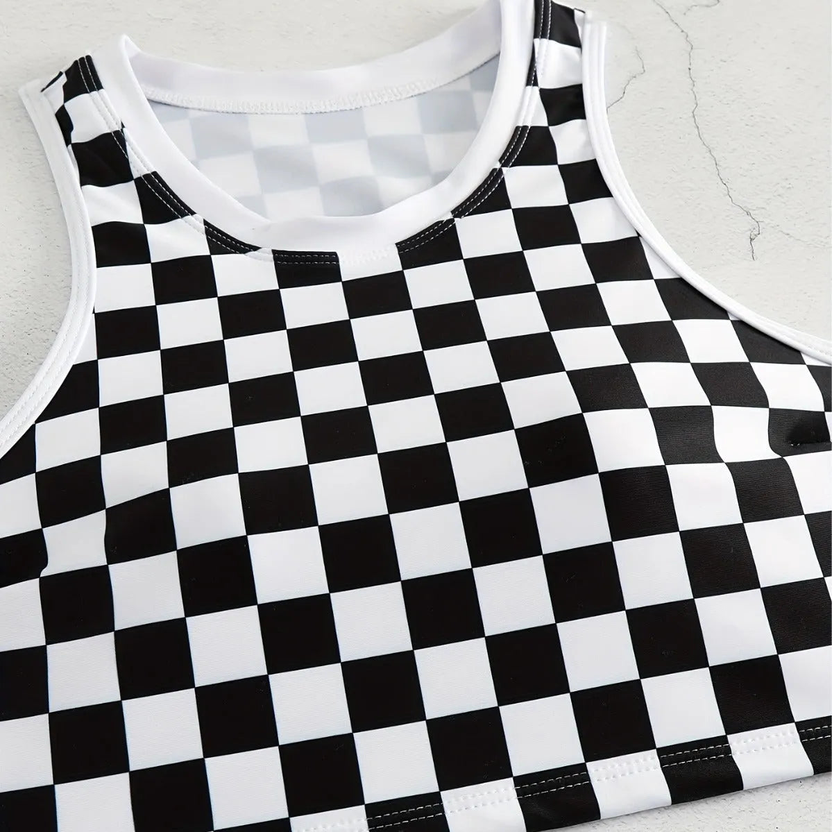 Adult woman wearing a black and white checkerboard print one-piece swimsuit with suspender straps and a backless sporty design.
