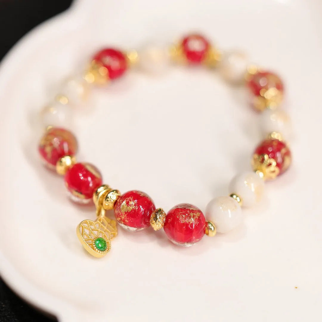 Women's ethnic style bracelet with gold foil designs on red and pink coloured glass glaze, featuring geometric shapes and charms.