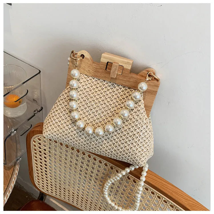 Women's woven straw shoulder bag with pearl chain detail showing horizontal square shape and internal compartments