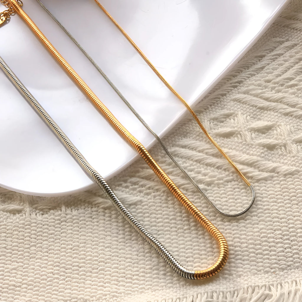 Close-up of a woman's golden 3mm wide snake bones chain necklace with geometric links.