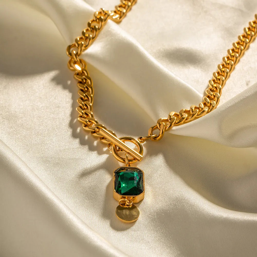 Gold titanium steel pendant necklace with geometric design and emerald zircon centre on Cuban link chain