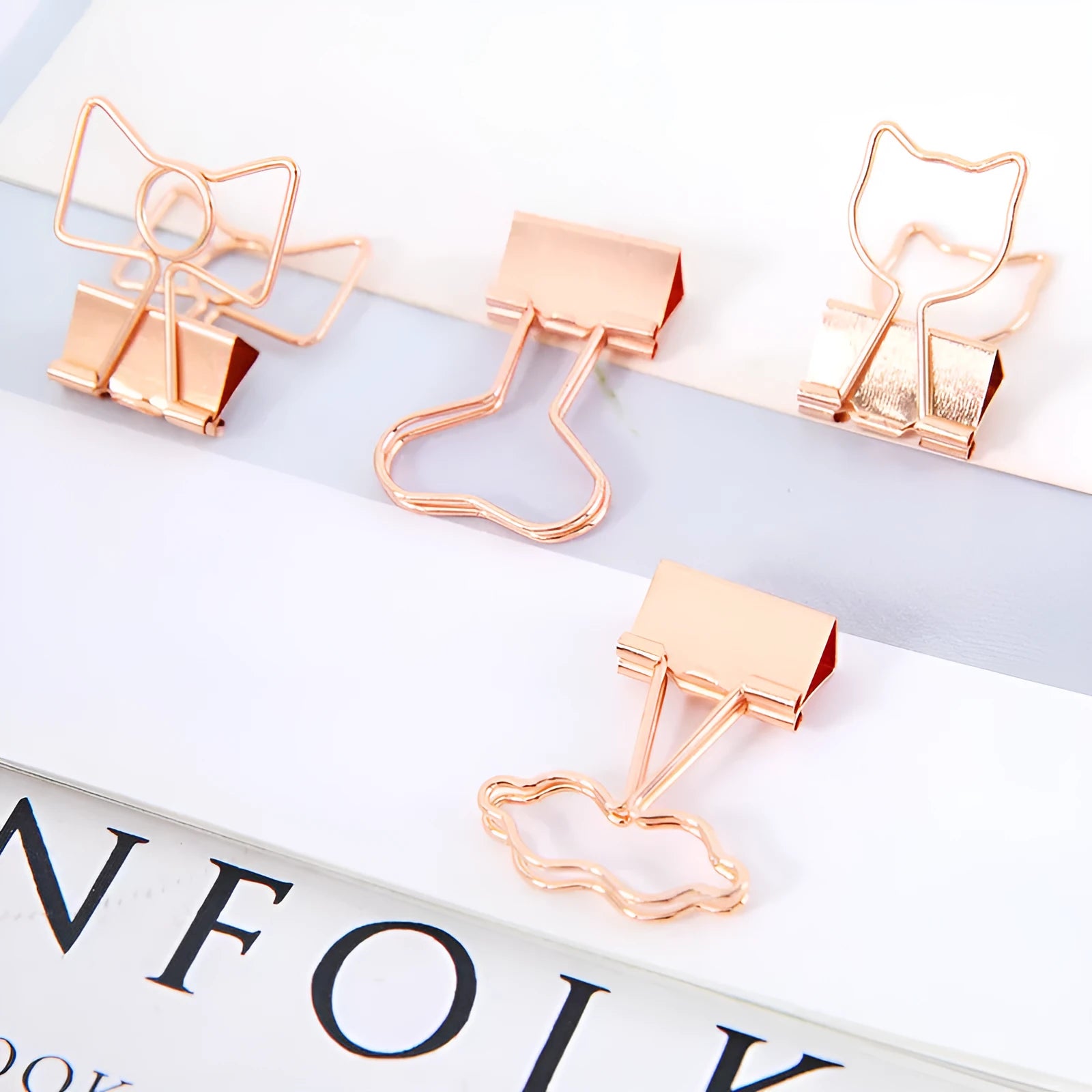 Small gold metal office clip with a decorative bow charm on a long tail.
