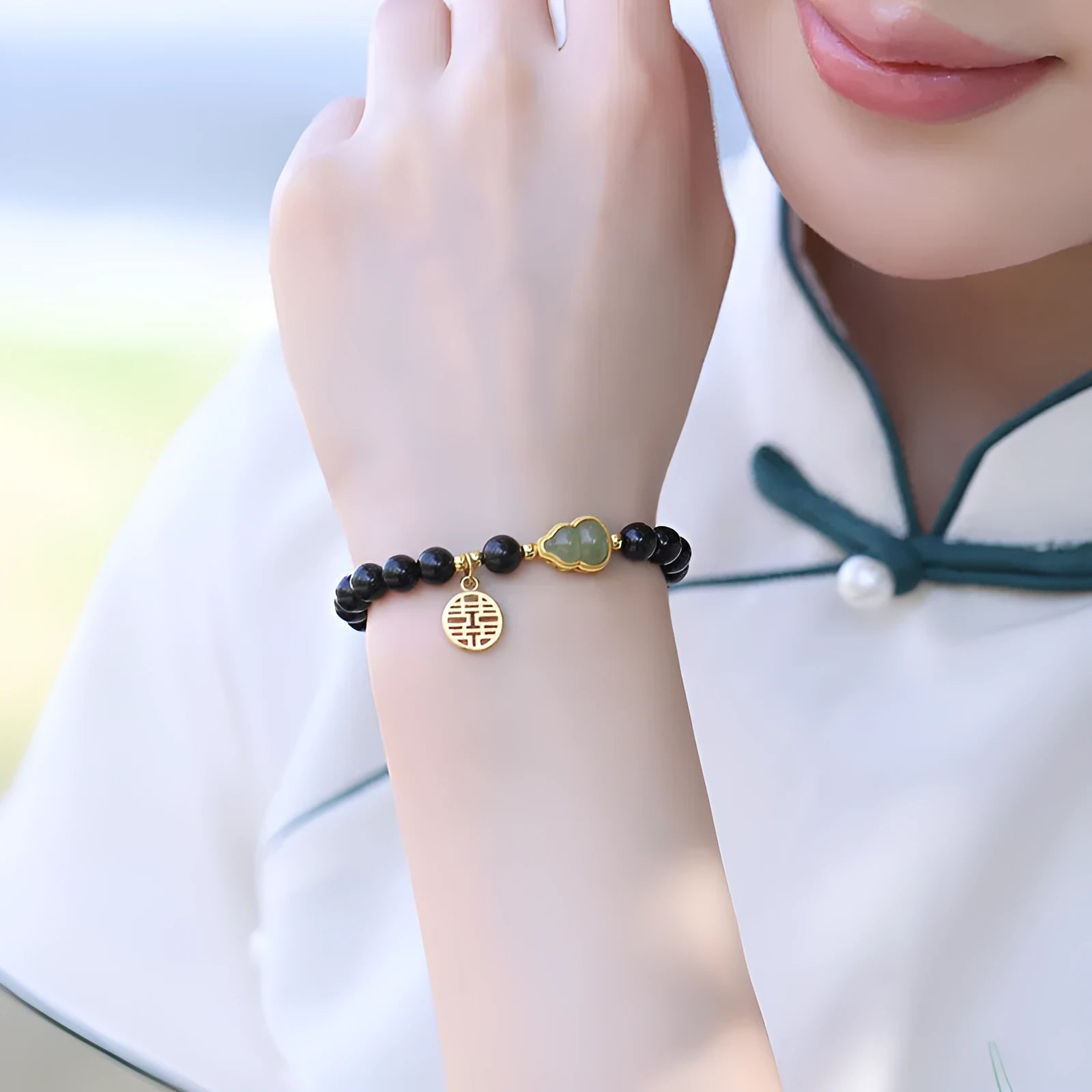 Black obsidian bracelet with a green Hetian jade gourd charm on a wrist.