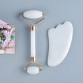 White jade double-headed facial roller and scraping board set on a flat surface.