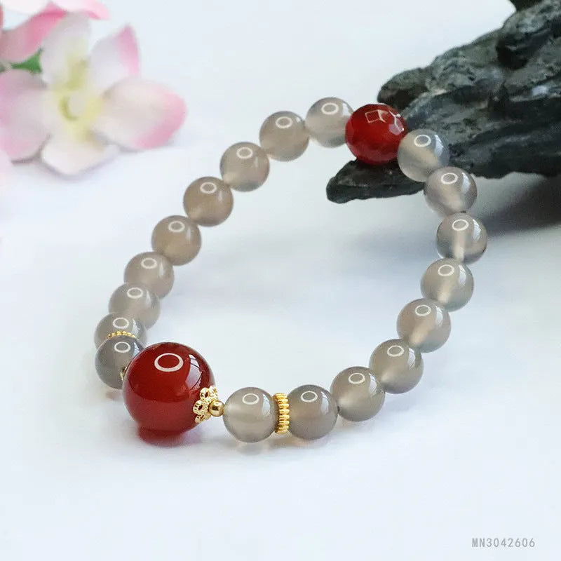 Close-up of a bracelet with smoky purple and red agate geometric beads on a white background.