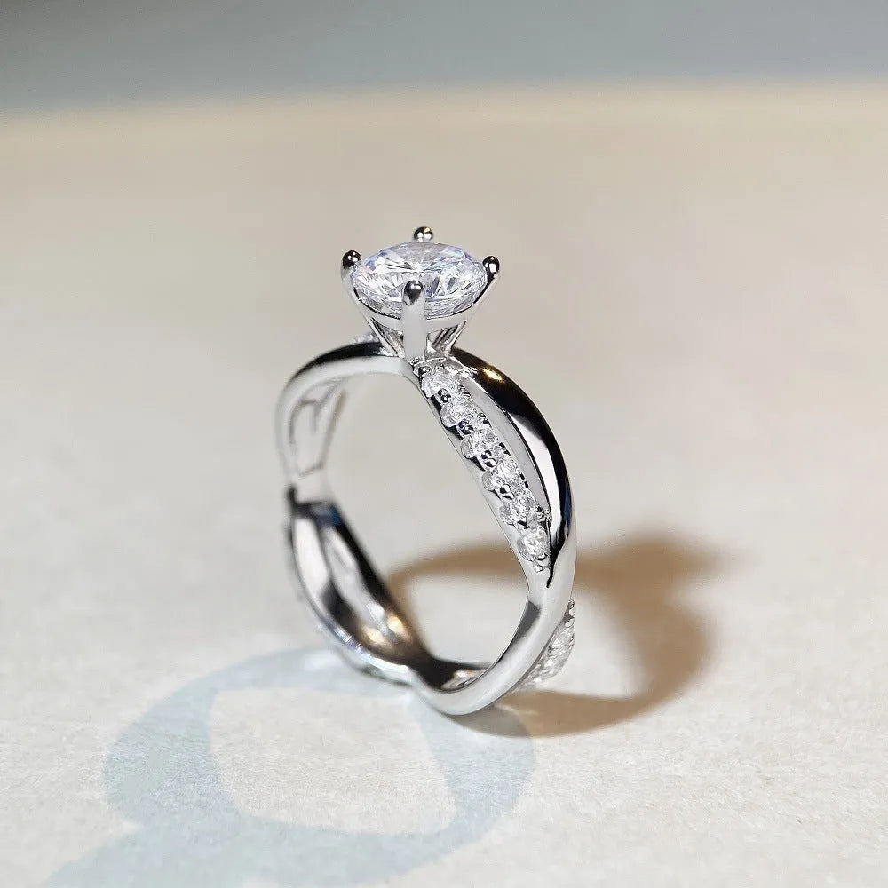 A silver moissanite ring with a 1 carat stone in a four-claw setting and a twisted geometric band.