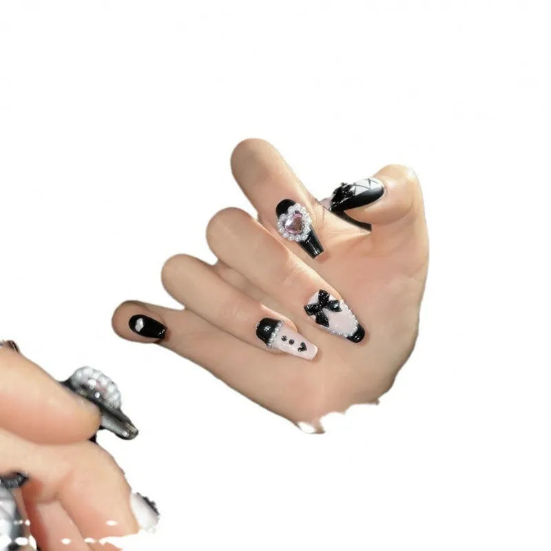 Hand-painted black artificial nails with pink hearts and a bow design, showing mid-length cat's eye style.