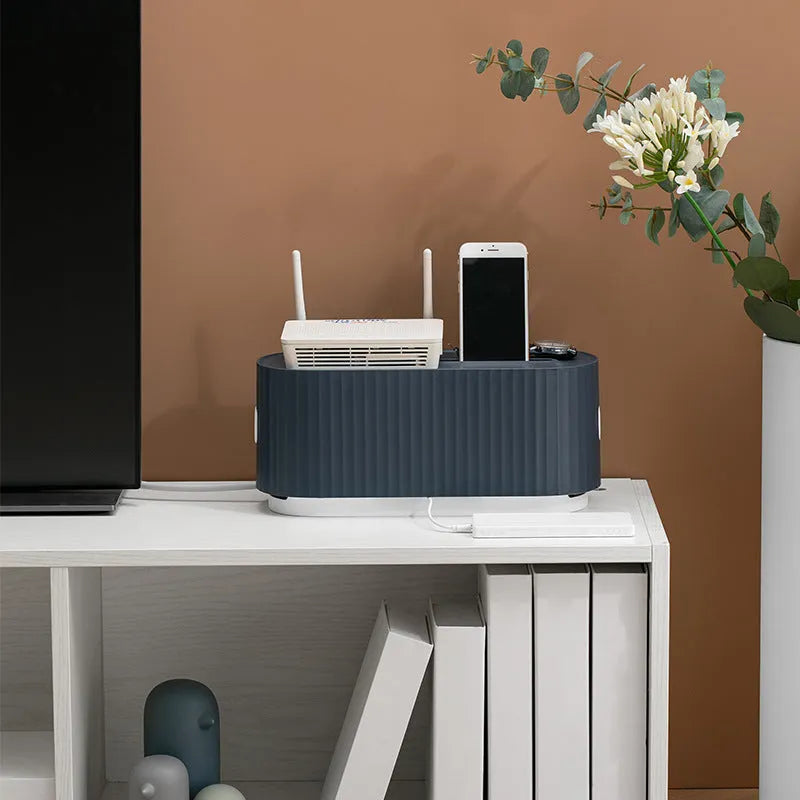 Blue and white plastic cable management box for power strips with lid open showing phone slot and cable holes