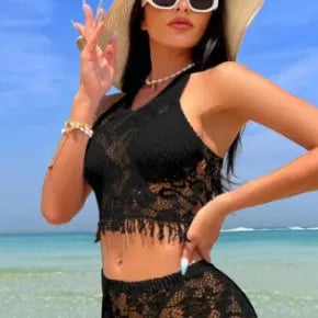 Women's white two-piece bikini with lace cover-up skirt and tassel trim on a beach.