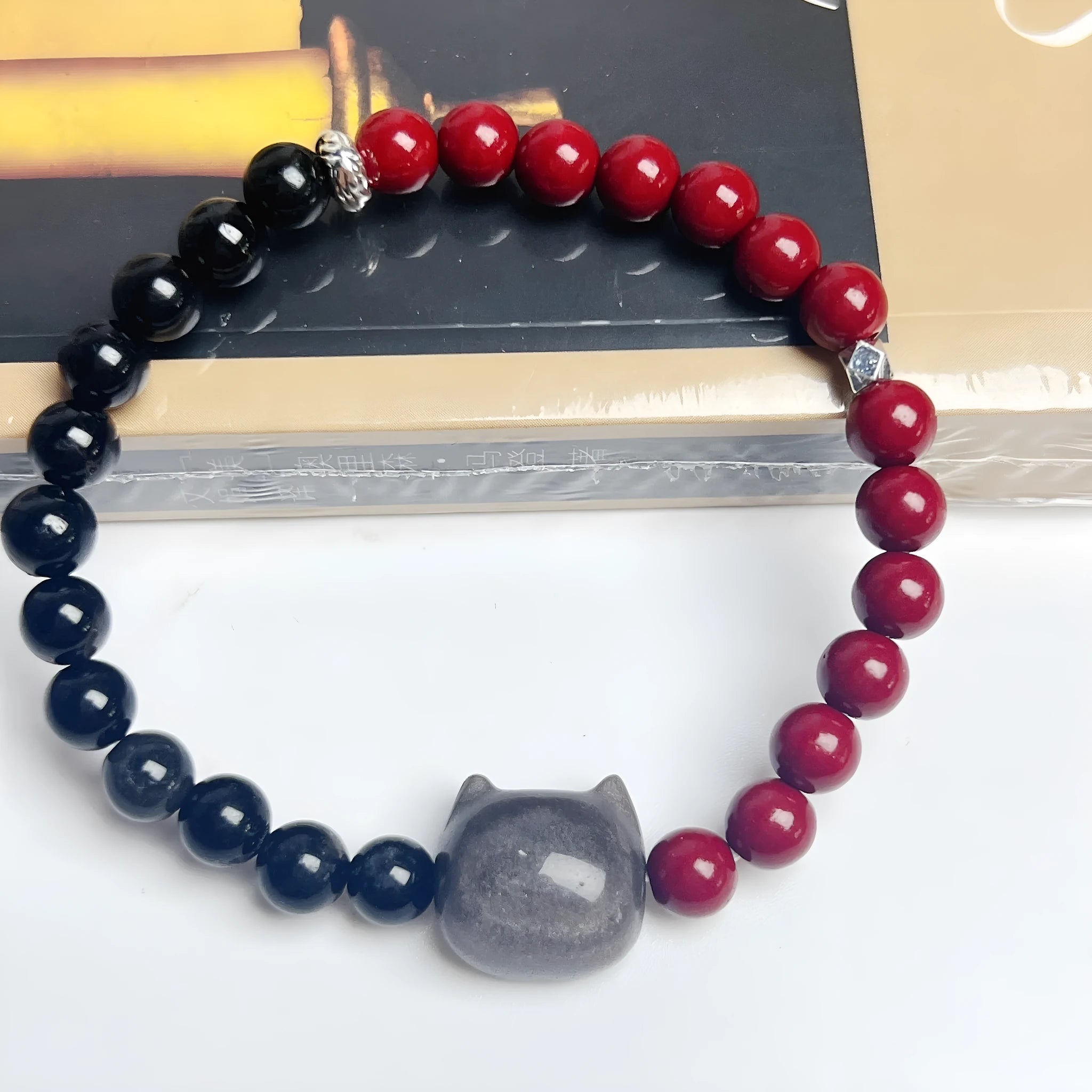 Handmade obsidian bead bracelet with a small cat charm on a cord.