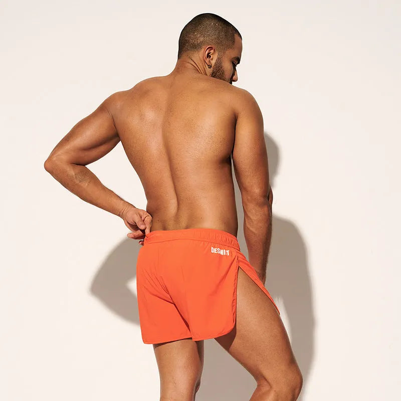 Men's loose orange red polyester beach surfing shorts with elasticated waist on a man