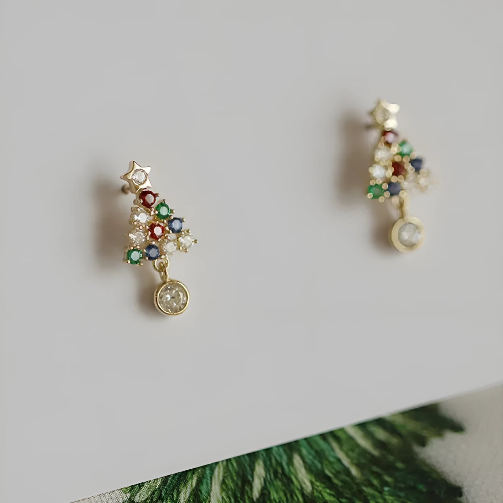 Gold Christmas stud earrings with diamond tree motif and water drop geometric shape on a light surface