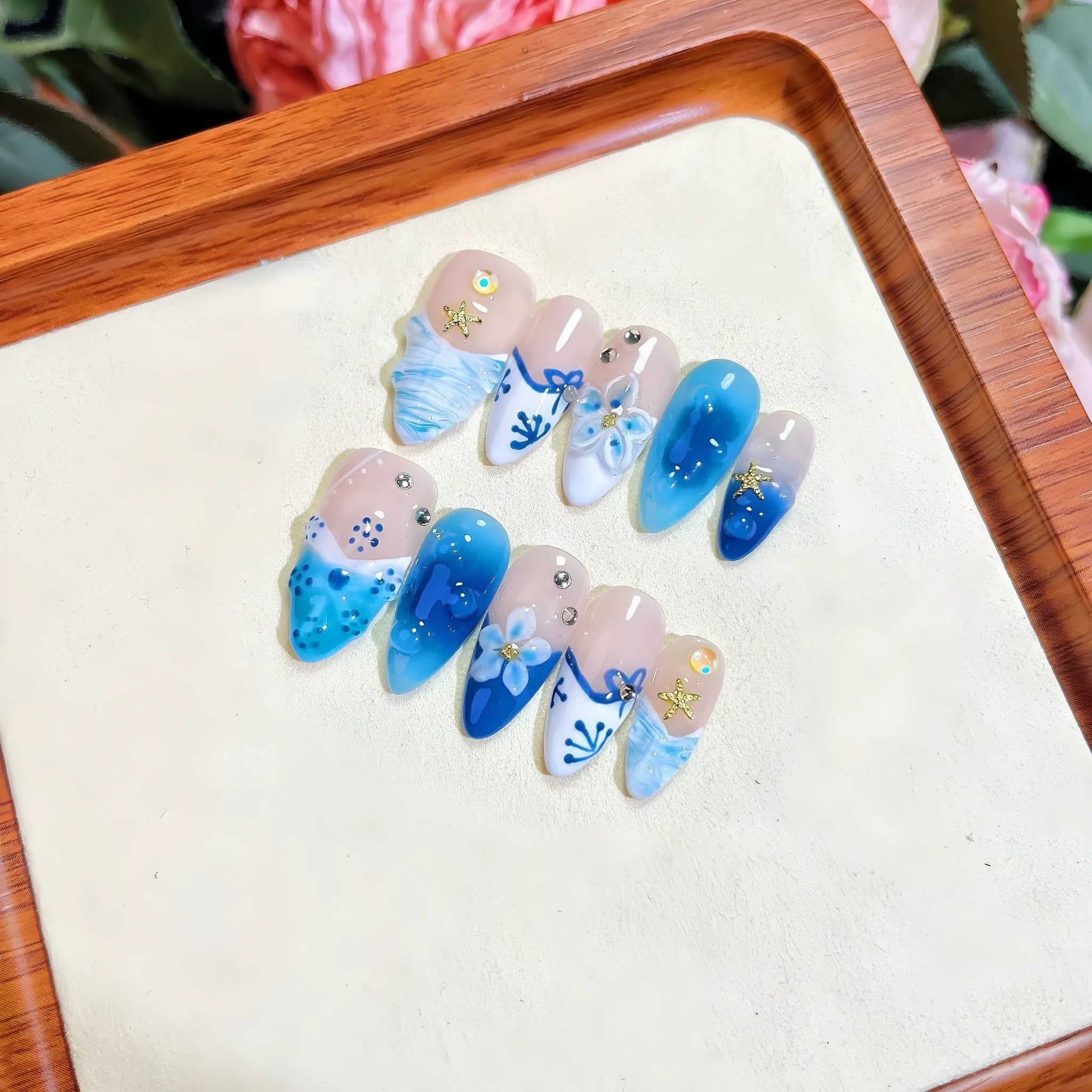 Set of blue false nails with hand-painted colour and carved summer ice design, laid out on a surface.