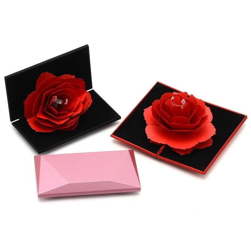 Red 3D heart-shaped plastic ring box with a rotating white rose decoration on top.