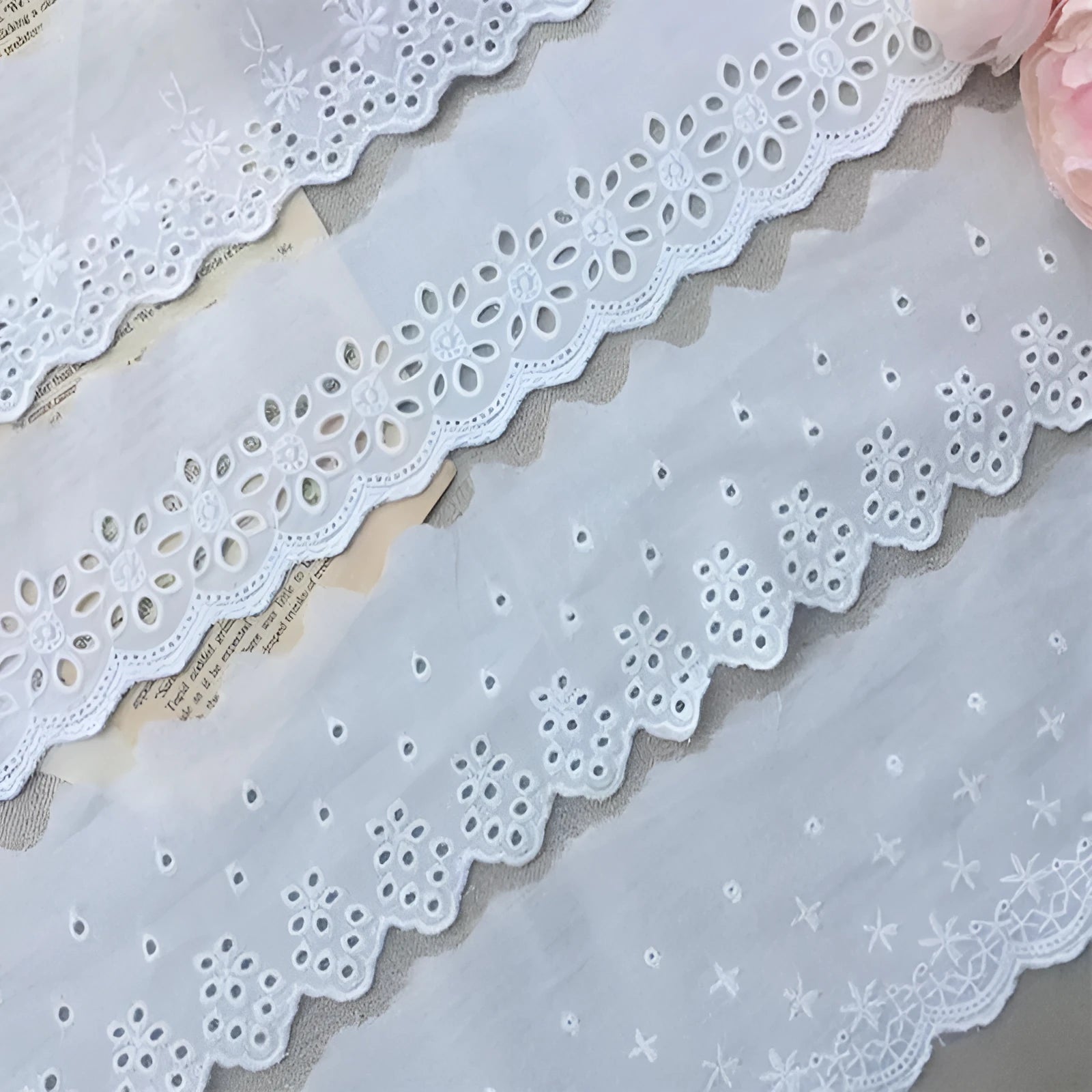 Roll of white cotton embroidery lace trim with cutout pattern, showing width variations.