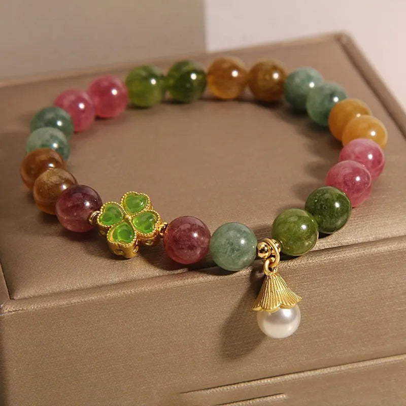 Natural colour tourmaline bracelet with four-leaf clover pearl pendant on wrist.
