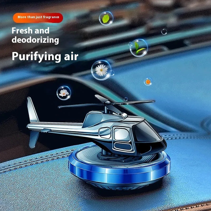 Silver metal solar-powered rotating helicopter car air freshener ornament on a dashboard.