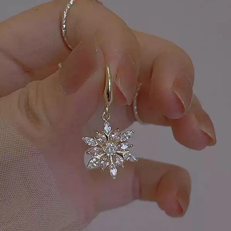 Gold alloy snowflake drop earrings with clear zircon centre on a white background