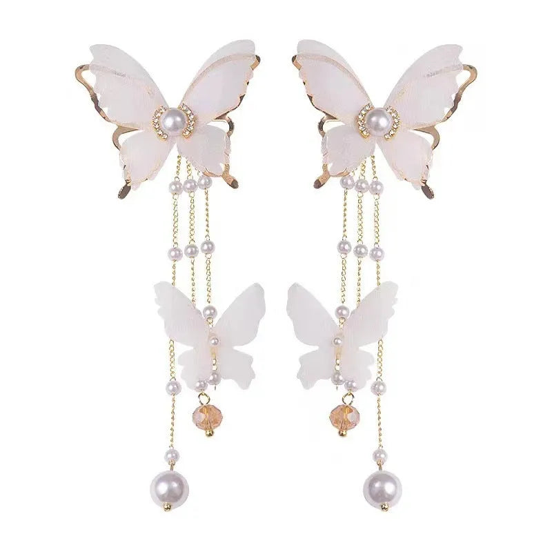Close-up of white butterfly-shaped earrings with dangling lace tassels and sparkling pearl rhinestone details.