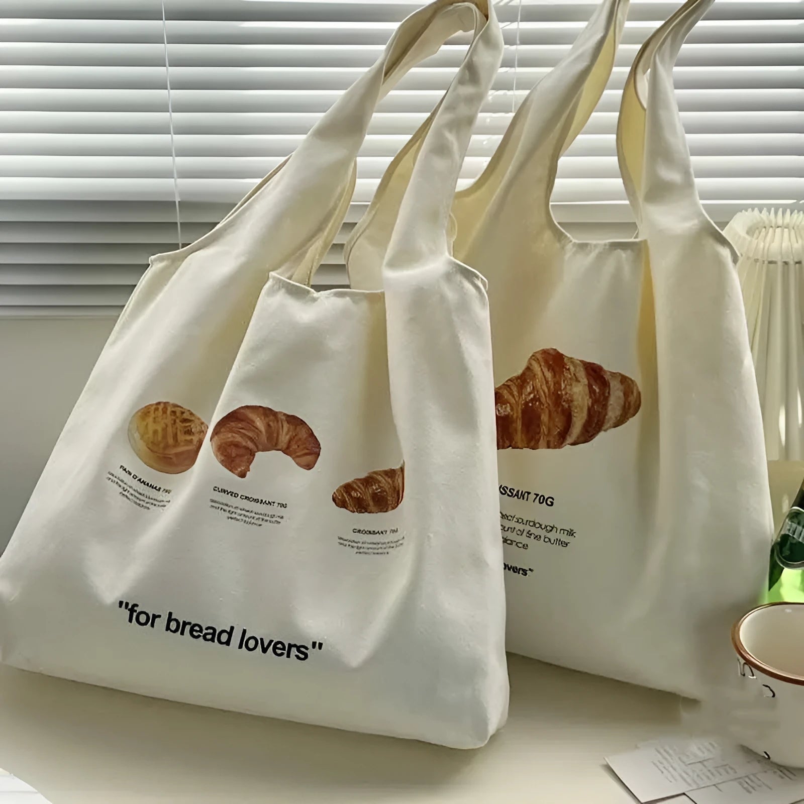 Beige canvas bag with bread patterns including croissant design, showing one-shoulder strap and structured form