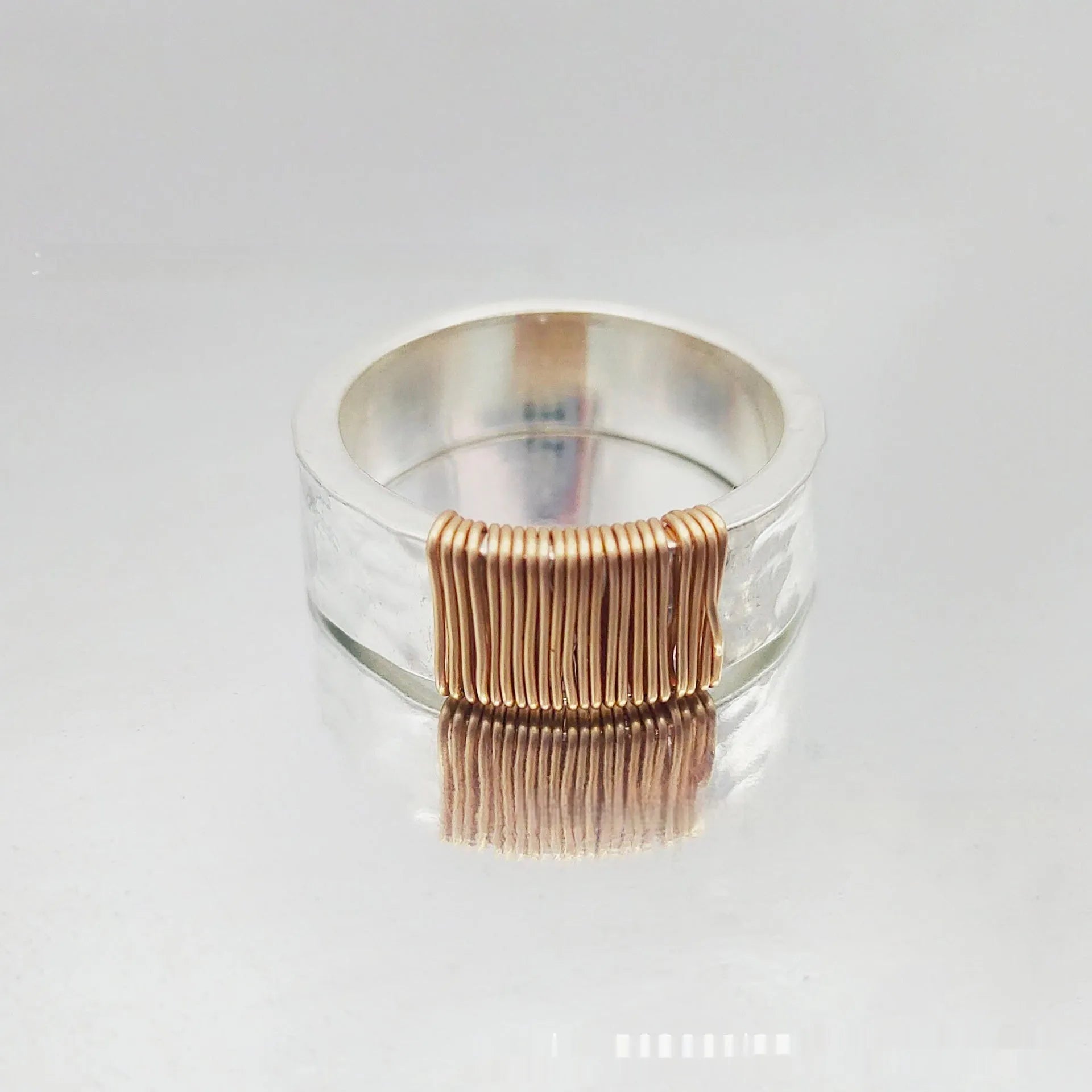 Copper wide face geometric ring bracelet in silver gold coil colour on a plain background.