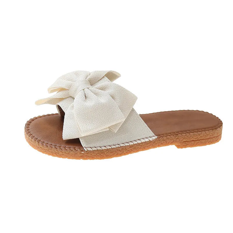 Women's beige suede slip-on sandals with a bow and flat soft rubber sole.