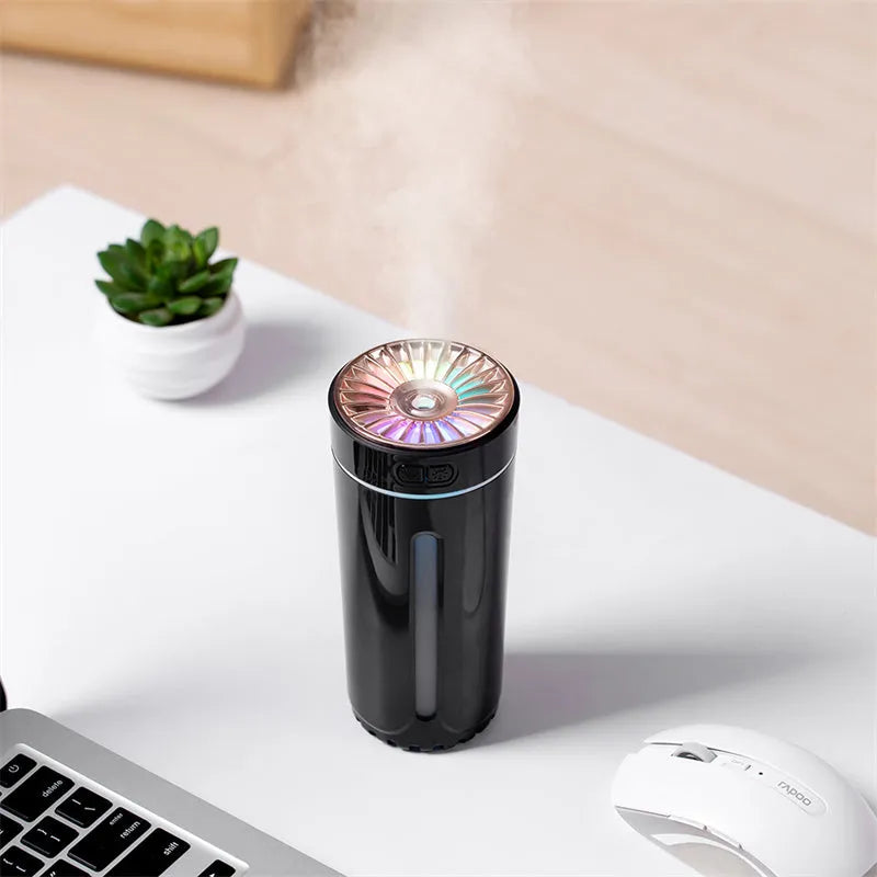 Black and white portable USB rechargeable car humidifier with colourful LED lights on a desk.