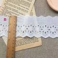 Roll of white cotton embroidery lace trim with cutout pattern, showing width variations.